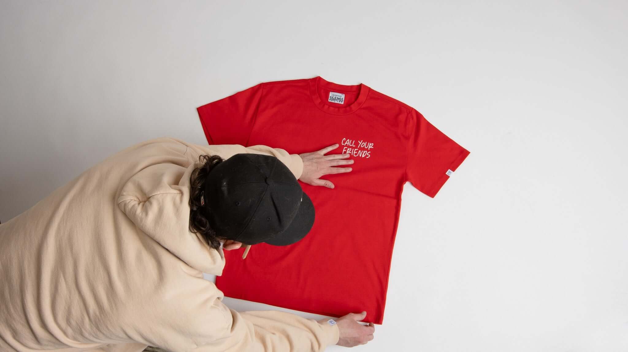 Person arranging a red CYF Tee made from 100% organic cotton, showcasing its soft and durable fabric, made in the USA.